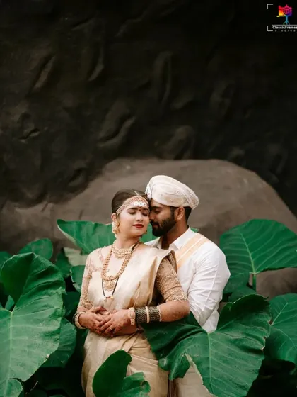 A tender moment captured amidst lush greenery. The couple's traditional white and gold outfits stand out beautifully against the natural backdrop, creating a serene and romantic portrait.