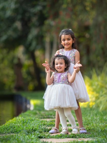 Two adorable sisters, dressed in matching outfits, posing by the water's edge. It's so wonderful to see their personalities shine during our outdoor kids' photoshoot.
