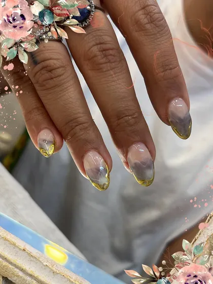 A beautiful set of nails with a smoky, watercolor base and a delicate gold chrome French tip. The floral edits add a whimsical touch to this artistic design.