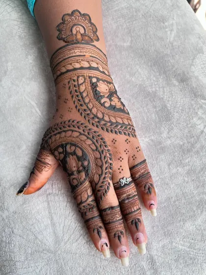 A close-up of one hand, highlighting the intricate circular mandala pattern and the delicate details on the fingers.