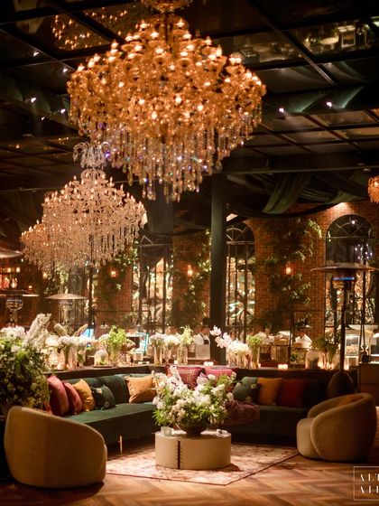 An overview of the lounge seating at the glass house reception. The space was filled with eclectic furniture, plush velvet sofas, and multiple crystal chandeliers, creating a sophisticated and glamorous atmosphere.