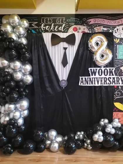 A creative tuxedo-themed backdrop for a work anniversary celebration. We design custom setups with balloon columns and foil numbers to make your internal office milestones memorable.