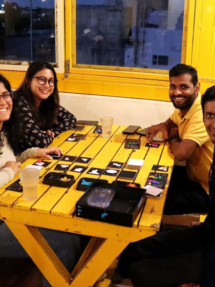 A group of friends enjoys a board game at our bright yellow table. The large windows provide a beautiful city view as they strategize and laugh together.