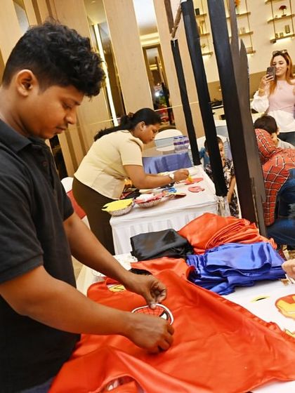 A staff member helps a young boy customize his superhero cape. I ensure there's enough help at each activity station so every child gets the attention they need.