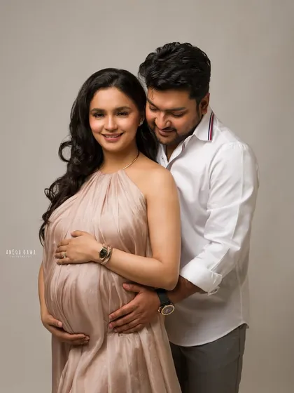 A warm and loving embrace. The soft, neutral tones of the gown and background complement the gentle and supportive connection between this expecting couple.