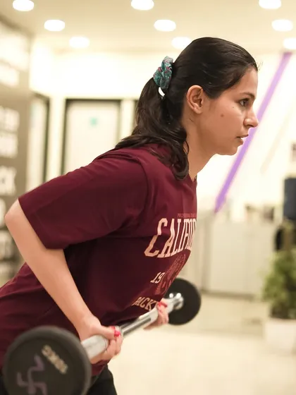 A member focuses on her form during a bent-over barbell row, an essential exercise for developing a strong and defined back.