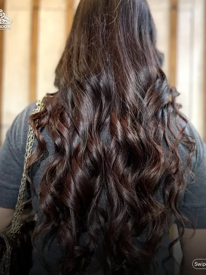 Showcasing voluminous, bouncy curls on long, dark hair. A professional blow-dry and curl service like this can completely transform your look for a day or night out.
