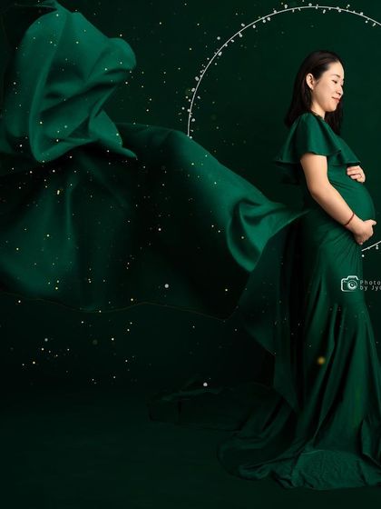 A creative edit of a mom-to-be in a green gown, surrounded by sparkles and a ring of light for a magical effect.
