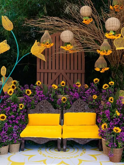 A closer look at the unique decor for a sunflower-themed Haldi. We pride ourselves on creative details, like this seating arrangement framed by vibrant purple blooms and custom-made sunflower installations, turning a traditional ceremony into a bespoke work of art.