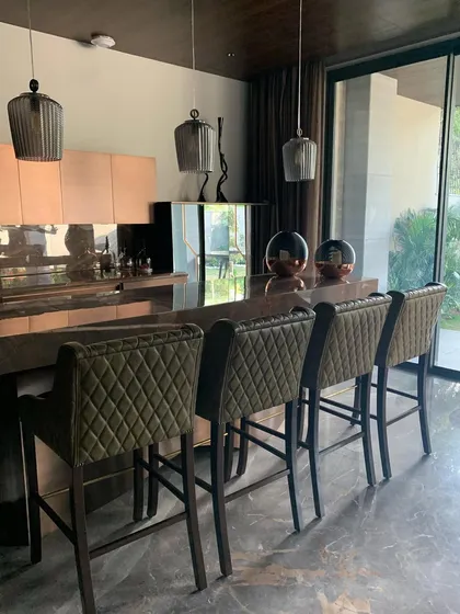 The warm and inviting palette of a home bar, featuring bronze and copper finishes, quilted leather bar stools, and smoked glass pendant lights. These details contribute to a sense of quiet luminosity and sophisticated comfort.