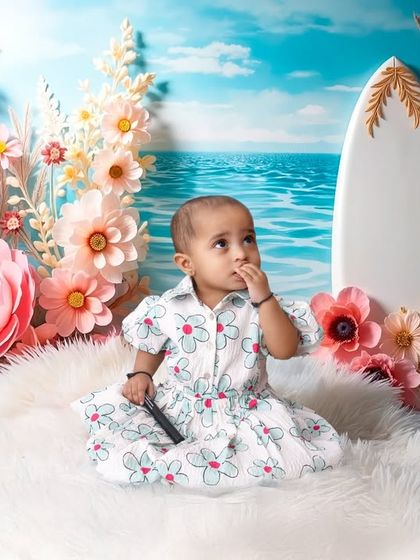 A wide shot of the beautiful beach setup, complete with a surfboard, a fluffy white rug for sand, and an elaborate arch of paper flowers against an ocean backdrop.