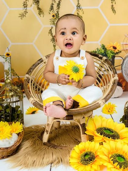 A baby boy holds a sunflower, looking up with a curious and sweet expression.