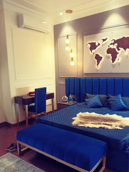 A bold and personalized bedroom design. This space features a striking royal blue upholstered bed and bench, complemented by a custom backlit world map, creating a unique and modern sanctuary for our client.