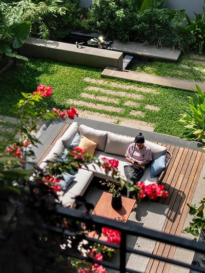 A high-angle shot of a woman relaxing on an outdoor sofa, surrounded by blooming flowers and greenery. This image captures the essence of creating personal, tranquil spaces within a larger family home.