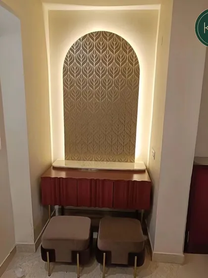 This unique setup features a floating console in a rich red finish, paired with two plush, neutral-toned ottomans. The backlit, leaf-patterned wall panel creates a warm and artistic focal point.