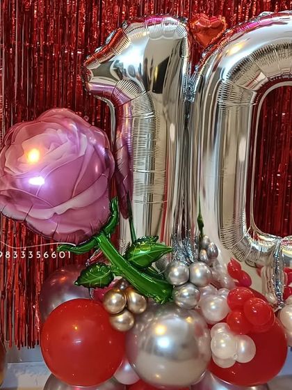A close-up of the base of the anniversary arrangement, featuring a large pink rose foil balloon alongside the silver '10' numbers, all built on a cluster of red and silver balloons.
