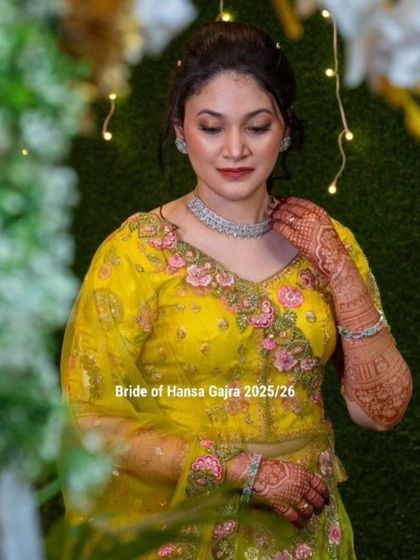 A full portrait of a bride wearing colored mehendi. The design on her hands and arms perfectly matches the floral embroidery on her yellow lehenga, creating a cohesive and stunning look.