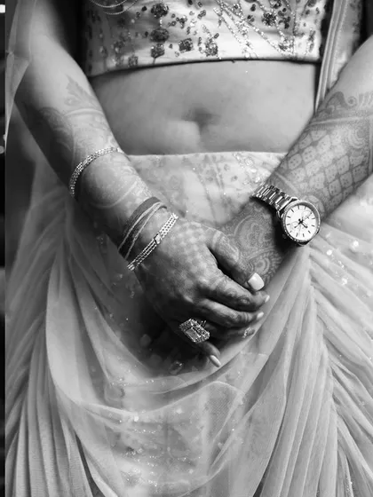 A black and white detail shot focusing on the bride's hands, adorned with mehendi and a modern watch. This artistic photo tells a story of tradition meeting modernity.