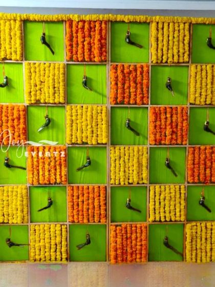 A unique and creative backdrop designed for a half saree function at home. We used a checkerboard pattern with panels of fresh marigolds and charming parrot hangings for a playful and traditional feel.