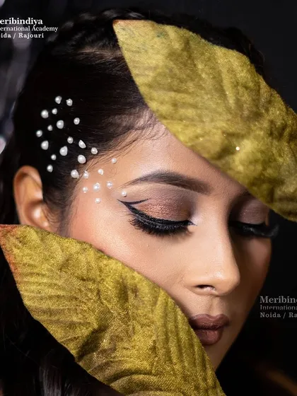An artistic shot using golden leaves to frame the face, highlighting the flawless cat-eye liner and soft brown eyeshadow.