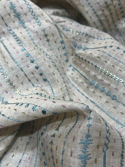 This linen fabric features delicate running stitches and sequin details, perfect for a subtle, elegant garment.