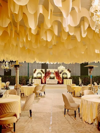 The full view of the elegant reception space, with the dramatic stage at one end and beautifully arranged guest seating under a canopy of white fabric.