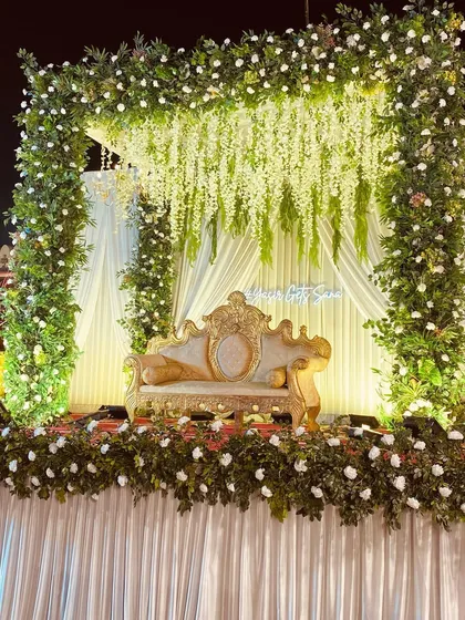 A classic reception stage with a full arch of greenery and white flowers. The hanging wisteria and custom neon sign add a personal, modern touch.