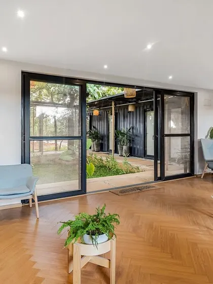 The interior of a marketing office built from a shipping container, featuring a spacious and modern waiting area. The large glass doors open up to a central courtyard, blending the workspace with nature.