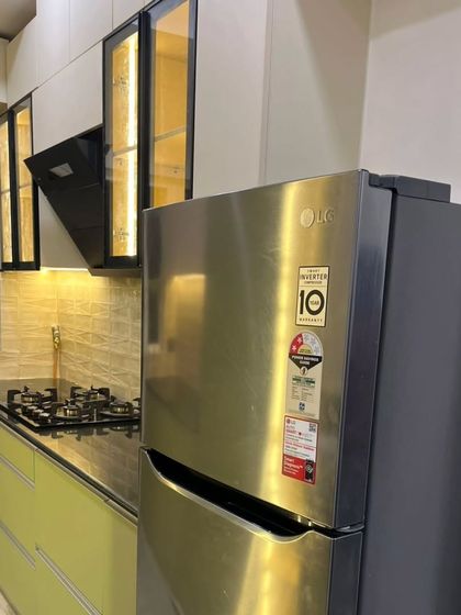 A modern modular kitchen at Mahagun Moderne, Noida. This design features a two-tone color scheme with light green base cabinets and off-white upper cabinets with profile handles.