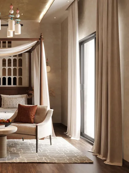 Natural light floods the room through a large glass door, illuminating the soft textures and earthy tones. The seating area provides a perfect spot to relax and enjoy the view.