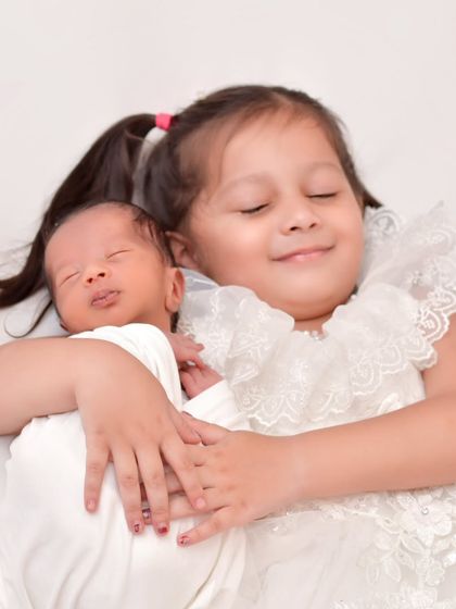A sweet and serene moment as an older sister cuddles her sleeping newborn sibling. The pure joy and peace on her face make this an incredibly heartwarming portrait.