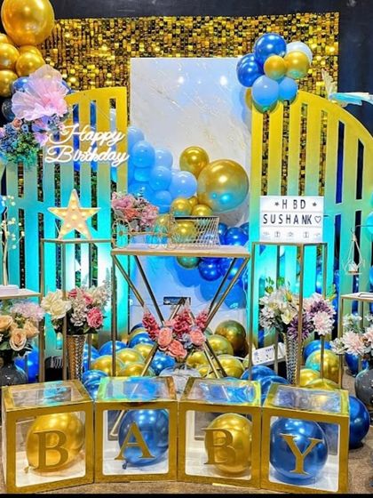 A vibrant blue and gold setup with a geometric backdrop, a gold shimmer wall, and "BABY" blocks filled with balloons.