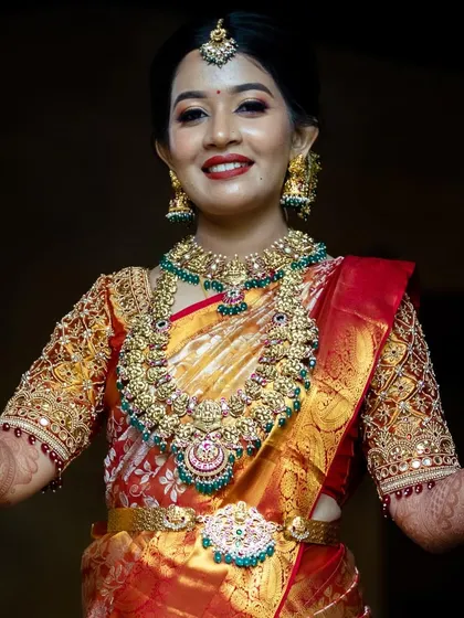 Our bride Bhoomika looks absolutely regal in her red and gold bridal saree, adorned with a grand, multi-layered temple jewellery set featuring green stone accents.