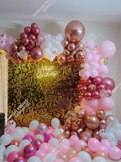 A luxurious birthday setup with a gold sequin wall and an elaborate balloon garland in shades of pink and rose gold.