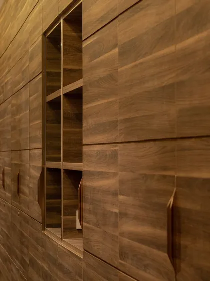 This full-wall wooden wardrobe is designed to be a feature in itself. The horizontal grain and integrated handles create a seamless look, while a central open niche breaks the monotony and provides space for display.