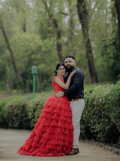A classic portrait from an engagement shoot in a lush Pune garden. The woman's striking red gown and the couple's confident pose create a timeless and elegant image, showcasing a more formal and styled approach to pre-wedding photography.