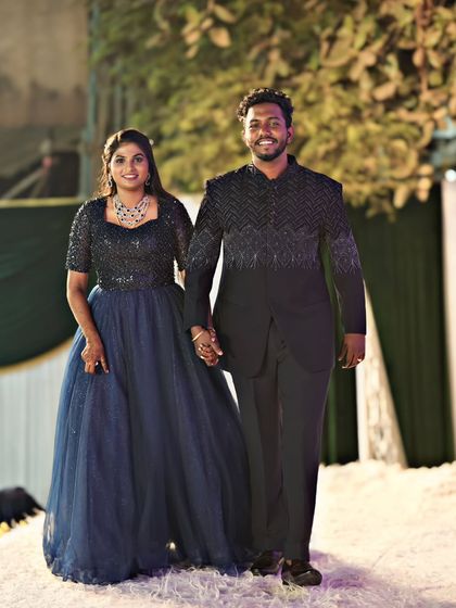 The full view of this stunning couple. The navy blue gown flows beautifully, while the groom's black Jodhpuri suit adds a touch of sharp, modern elegance.