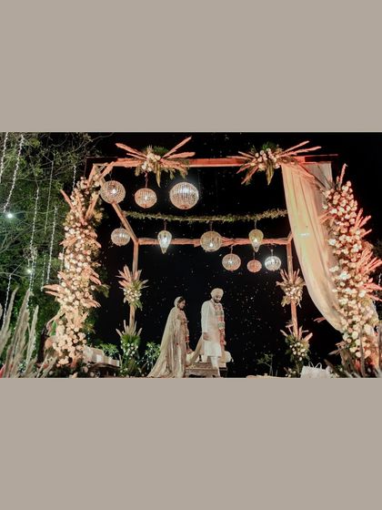 A wide shot of the couple at their beautifully decorated mandap at night. The stunning floral and light decor creates a magical ambiance for their wedding ceremony.