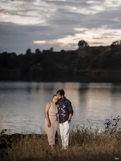 A serene and moody portrait of Prem and Jinal by a lake at dusk. The dramatic sky and calm water create a beautiful, cinematic backdrop for their quiet moment of togetherness.