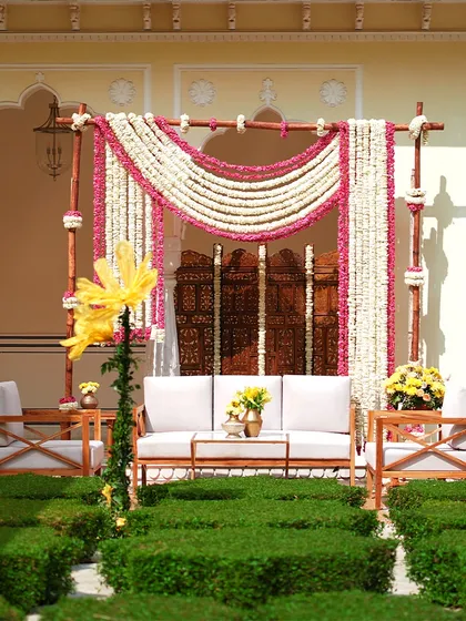 A traditional Haldi setup with a backdrop of fresh jasmine and marigold curtains. The antique wooden screen adds a touch of rustic elegance.