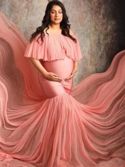 A studio shot of a client in a beautiful peach mermaid gown with a flowing tulle cape. The fabric drapes beautifully, creating a sense of movement and grace.