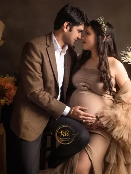 A romantic seated portrait of a couple. They are surrounded by a rustic, candlelit setting with pampas grass and floral arrangements, creating a warm and intimate atmosphere.