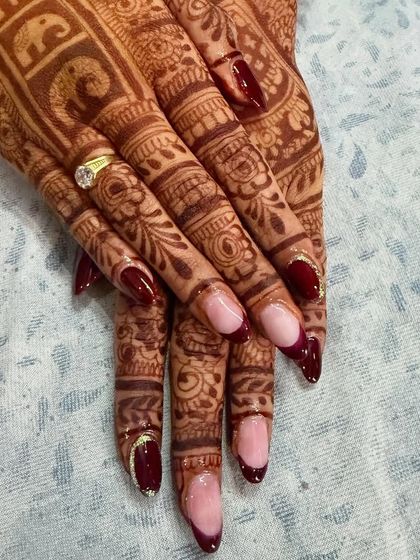 This close-up shows the detail of the deep red reverse French manicure against the beautiful bridal henna. The subtle gold glitter line adds a touch of elegance.
