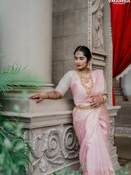 An elegant bridal portrait of a bride in a beautiful pink saree, posing by a pillar. We take the time to capture stunning solo portraits.