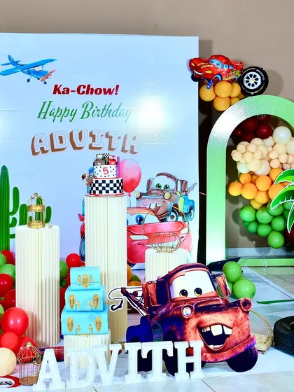 A close-up of the main backdrop for Advith's party, featuring Mater and the phrase "Ka-Chow! Happy Birthday." The checkered flag cake sits on a custom plinth.
