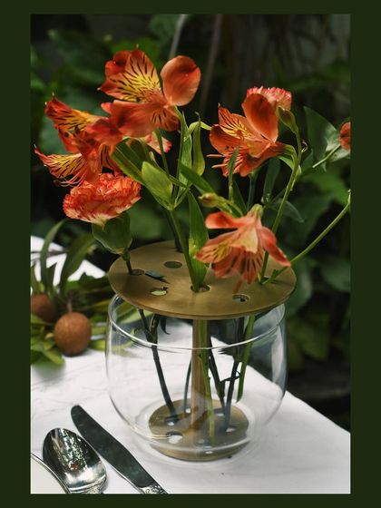 A close-up of a unique glass and brass Ikebana-style flower vase from Byaas Home. This shot focuses on the product's thoughtful design, showing how it elegantly holds each stem.
