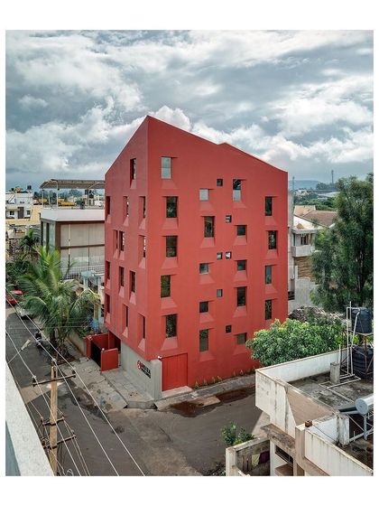 An aerial perspective of the "Stacked Student Housing" shows how the building occupies its corner plot. The monolithic red form stands out in the residential suburb, redefining the neighborhood's skyline.