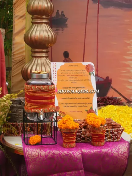 A traditional welcome drink station with marigold decorations and a personalized note for guests, set against a Banaras ghat backdrop.