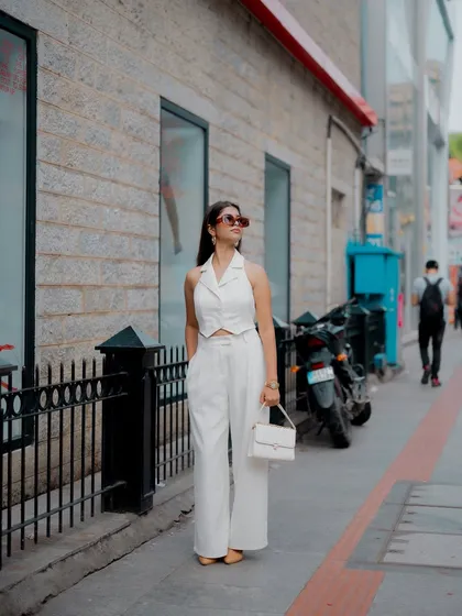 A full-length shot of a model in a chic white outfit, walking down a city street. This captures a natural, candid moment of urban style.
