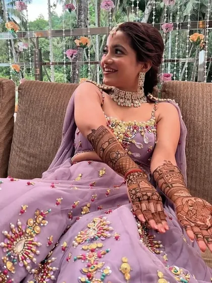 A beautiful bride in a lavender lehenga, smiling as she shows her intricate bridal mehendi.
